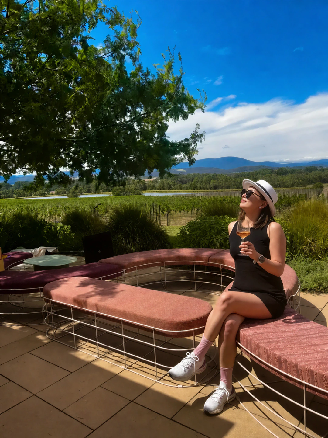 Alicia in a black dress and white hat seated at a Yarra Valley winery